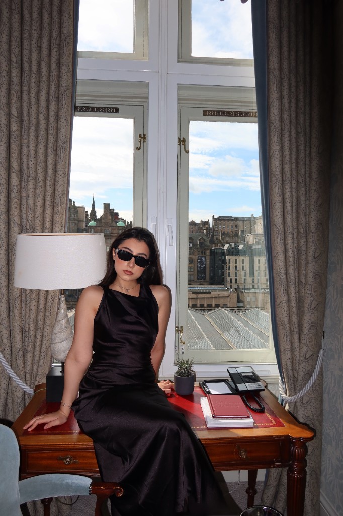 Look 1 — Black satin dress, seated at the window